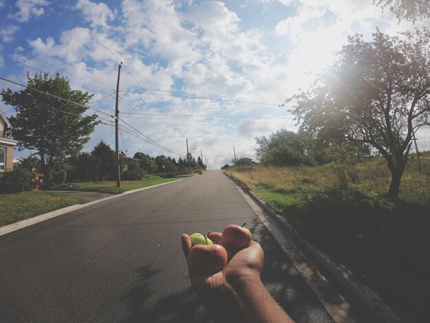 Foto pessoa segurando maçãs na estrada contra o céu