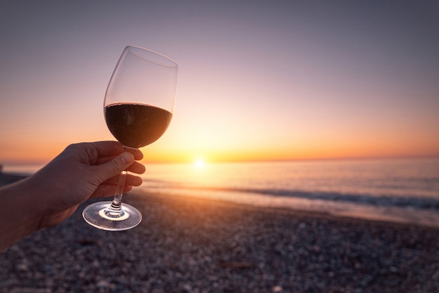 Pessoa, segurando o copo de vinho tinto durante assistir o pôr do sol e desfrutar de férias no mar