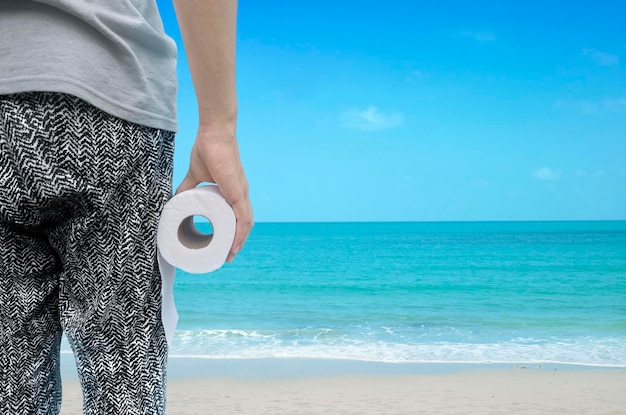 Pessoa segurando rolo de papel higiênico em pé na praia