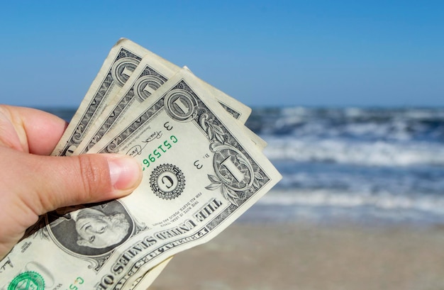 Pessoa segurando três notas de dólar de papel no fundo do mar e ondas do mar