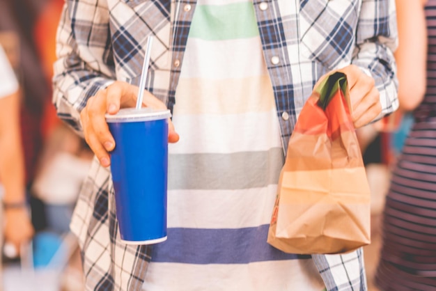 Pessoa segurando um pacote de fast food e copo com almoço em público