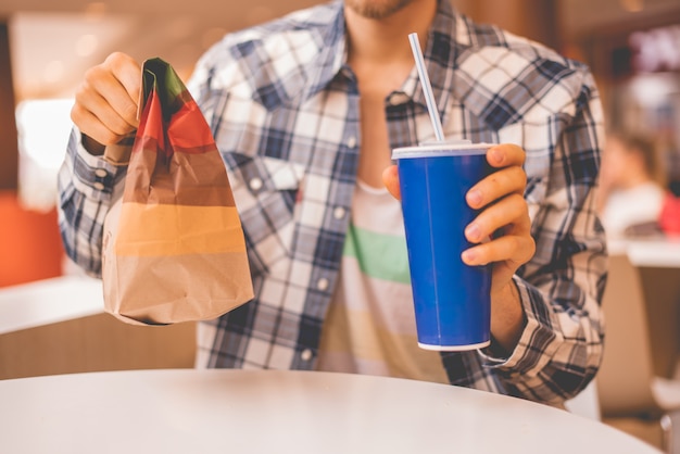 Pessoa segurando um pacote de fast food e um copo com almoço em público