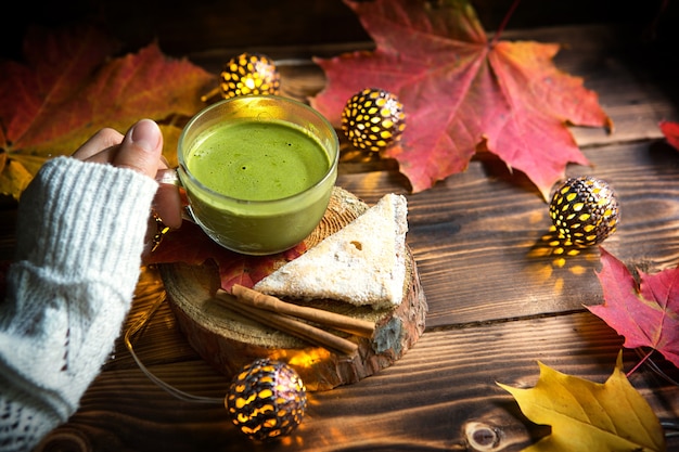 Pessoa segurando uma xícara de chá matcha com decoração de outono