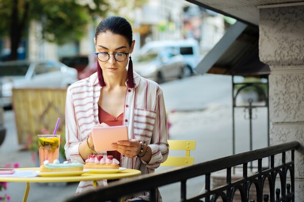 Pessoa séria. Mulher calma olhando atentamente para a tela de um tablet moderno enquanto está sentada em um café ao ar livre