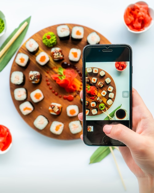 Foto pessoa tira uma foto de sushi em uma superfície redonda de madeira com gengibre