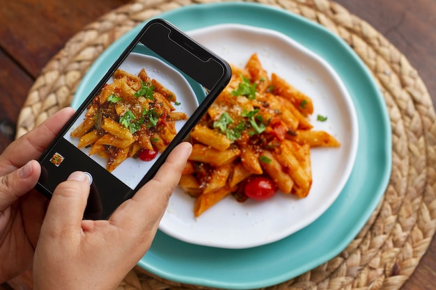 Foto pessoa tirando foto de prato de macarrão com smartphone