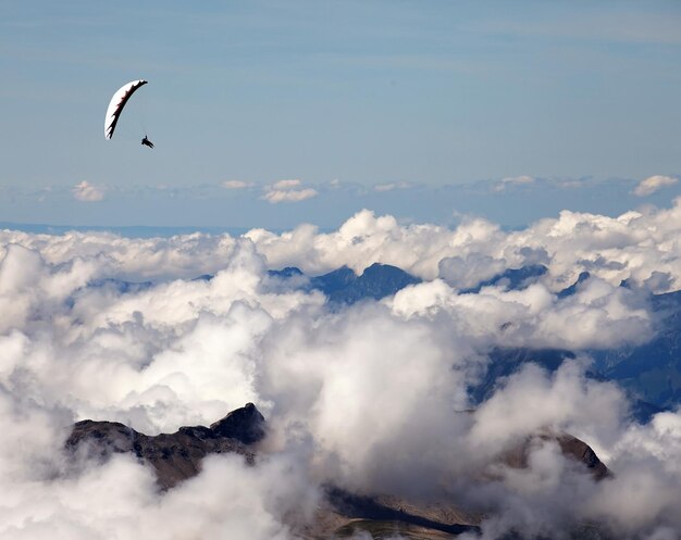 Pessoa voando de parapente sobre o cenário nublado contra o céu azul nos Alpes suíços