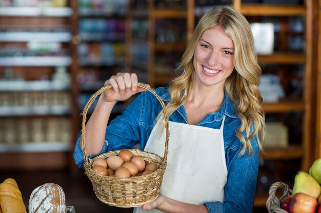 Pessoal feminino sorridente segurando cesta de ovo no supermercado