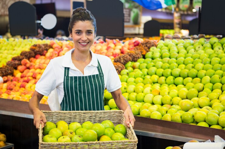 Foto pessoal feminino sorridente segurando uma cesta de maçã verde no supermercado