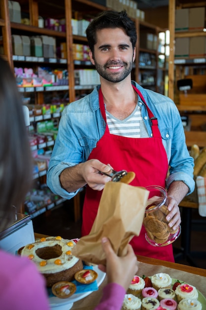 Pessoal masculino sorridente colocando biscoitos no saco de papel