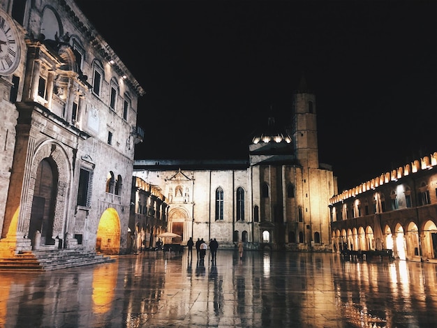 Pessoas a caminhar entre edifícios à noite.