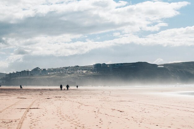 Foto pessoas a caminhar na praia contra o céu nublado