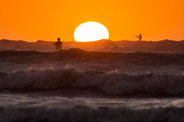 Pessoas a fazer kitesurf no mar contra o céu