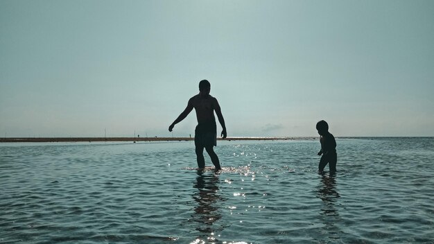 Pessoas a vadear o mar contra um céu limpo