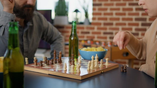 Jovens se divertindo com jogos de tabuleiro de xadrez, servindo bebidas  alcoólicas e lanches. grupo de amigos jogando partida na mesa para  entretenimento na reunião. tiro de tripé. fechar-se.