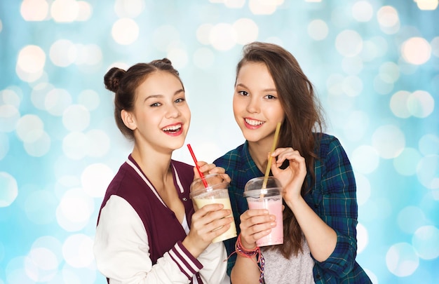 pessoas, amigos, adolescentes e conceito de amizade - felizes e sorridentes lindas adolescentes bebendo milk-shakes e com palha sobre fundo azul de luzes de férias