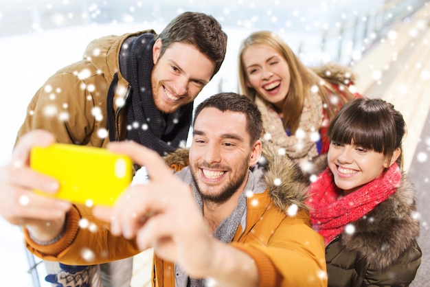 pessoas, amizade, tecnologia e conceito de lazer - amigos felizes tomando selfie com smartphone na pista de patinação