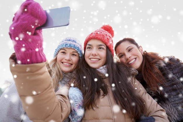 pessoas, amizade, tecnologia, inverno e conceito de lazer - adolescentes felizes tomando selfie com smartphone ao ar livre