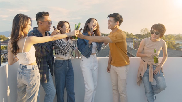 Pessoas asiáticas bebendo álcool na festa do pôr do sol no telhado amigos asiáticos tilintando com garrafa de cerveja
