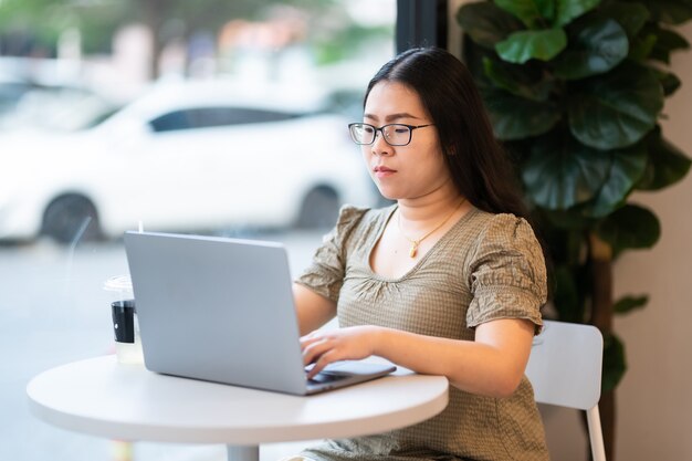 Pessoas asiáticas freelance de negócios feminino casual trabalhando com um computador laptop com uma xícara de café e smartphone na cafeteria como o plano de fundo, o conceito de comunicação