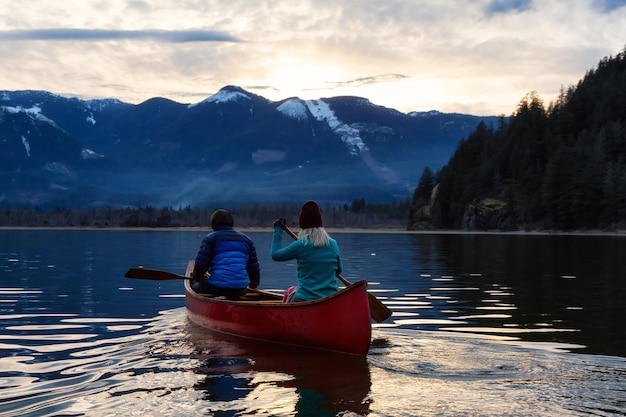 Pessoas aventureiras em uma canoa de madeira estão curtindo a paisagem montanhosa canadense