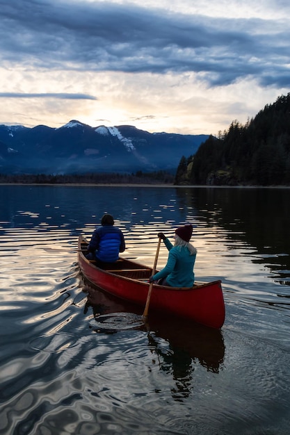 Pessoas aventureiras em uma canoa de madeira estão curtindo a paisagem montanhosa canadense