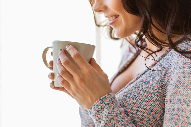 pessoas, bebidas e conceito de lazer - close-up de uma jovem feliz com uma xícara de chá ou café em casa