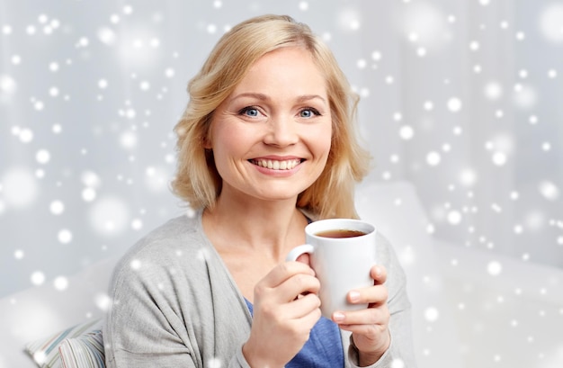 pessoas, bebidas e conceito de lazer - mulher sorridente com uma chávena de chá ou café em casa sobre a neve
