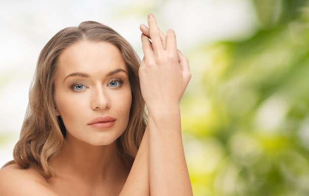 pessoas, beleza, corpo e conceito de cuidados com a pele - rosto de mulher bonita e mãos sobre fundo verde