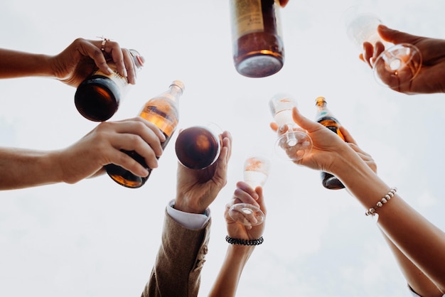 Pessoas brindando com bebidas em copos e garrafas contra o céu