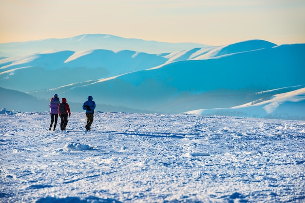 Pessoas caminhando ao pôr do sol nas montanhas de inverno cobertas de neve