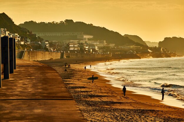 Foto pessoas caminhando na praia contra o céu durante o nascer do sol