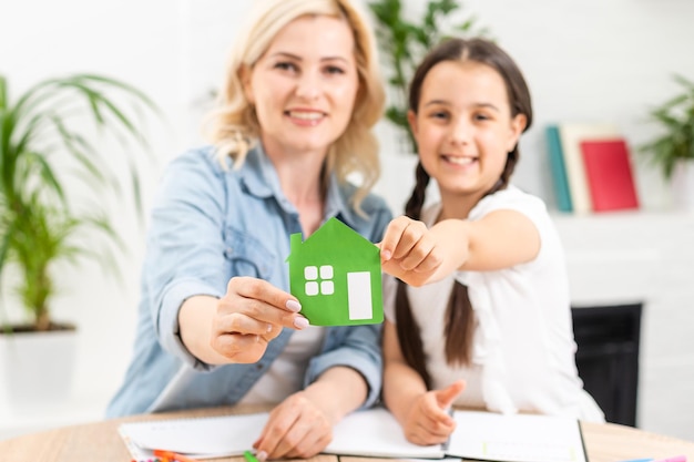 Foto pessoas, caridade, família e conceito de casa - close-up de mulher e menina segurando recorte de casa de papel verde nas mãos em concha.