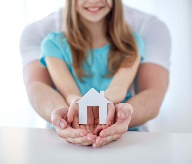 Foto pessoas, caridade, família, imóveis e conceito de casa - close-up de homem e menina segurando recorte de casa de papel verde nas mãos em concha