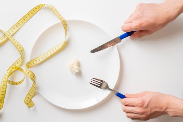 Pessoas com as mãos com garfo e faca comem uma pequena porção de comida. anorexia b