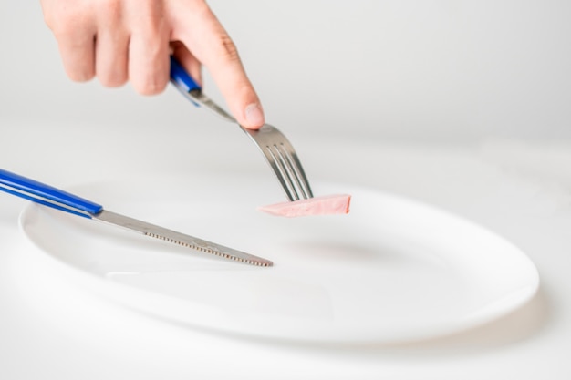 Pessoas com as mãos com garfo e faca comem uma pequena porção de comida. anorexia b