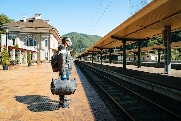 Pessoas com máscara na estação ferroviária contra montanhas e céu