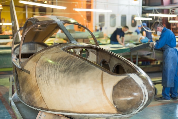 Pessoas com roupas azuis constroem um avião na fábrica. Trabalhadores de macacão trabalhando nos detalhes da aeronave.