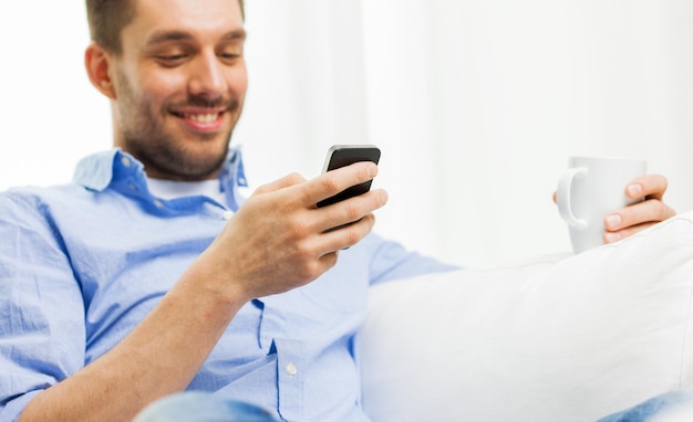 pessoas, comunicação, tecnologia e conceito de internet - close-up de homem sorridente com mensagens de texto de smartphone ou mensagem de leitura e bebendo chá em casa