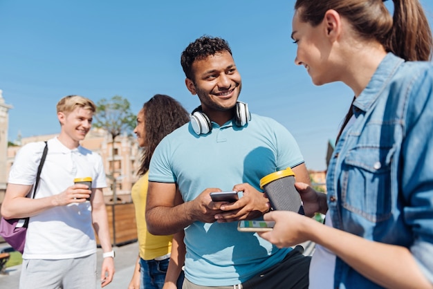 Pessoas comunicativas. Homem positivo com um sorriso no rosto e segurando o telefone enquanto olha para o amigo