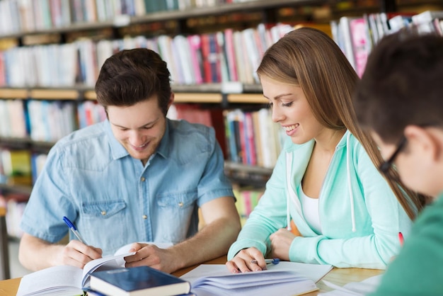 pessoas, conhecimento, educação e conceito de escola - grupo de estudantes felizes com livros se preparando para exame na biblioteca