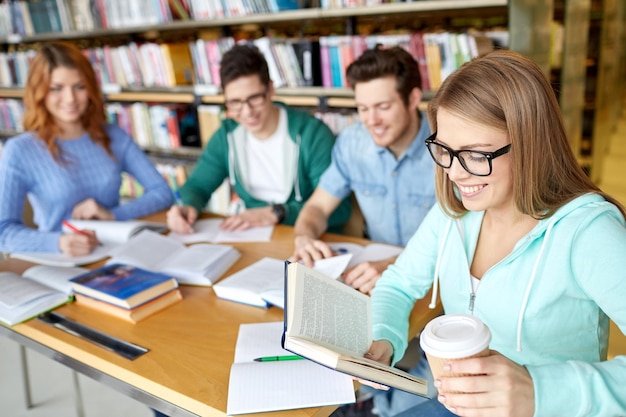 pessoas, conhecimento, educação e conceito de escola - grupo de estudantes felizes lendo livros, bebendo café e se preparando para o exame na biblioteca