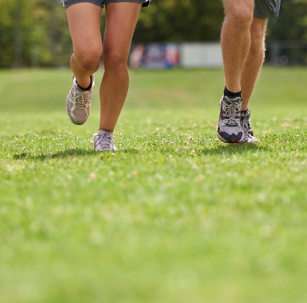 Foto pessoas correndo sapatos e close-up na grama para treino juntos no verão para saúde bem-estar ou treinamento pessoa corredor e parceiro com pés no campo para exercício aptidão e velocidade com tênis