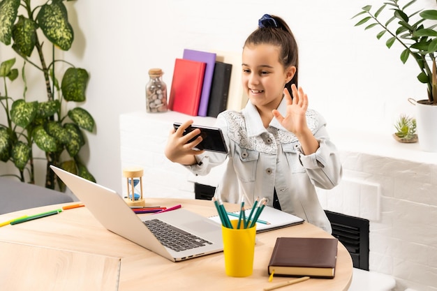 pessoas, crianças e conceito de tecnologia - menina com computador portátil e smartphone tirando selfie ou fazendo videochamada em casa