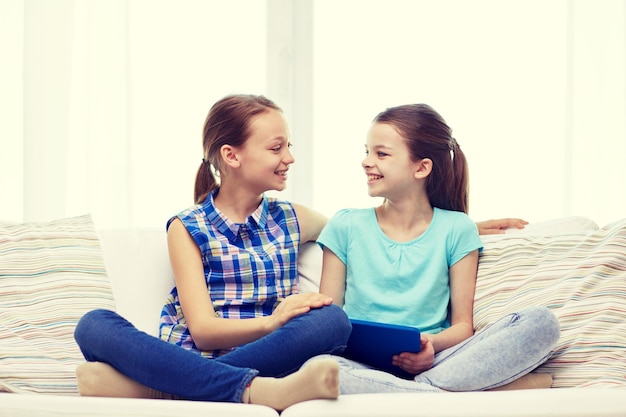 pessoas, crianças, tecnologia, amigos e conceito de amizade - meninas felizes com computador tablet pc sentado no sofá e conversando em casa