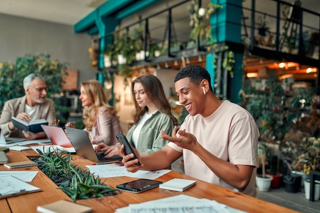 Pessoas criativas multirraciais em um escritório moderno. grupo de jovens empresários e chefe sênior estão trabalhando juntos com laptop, tablet, smartphone, caderno, gráficos. equipe de sucesso em coworking