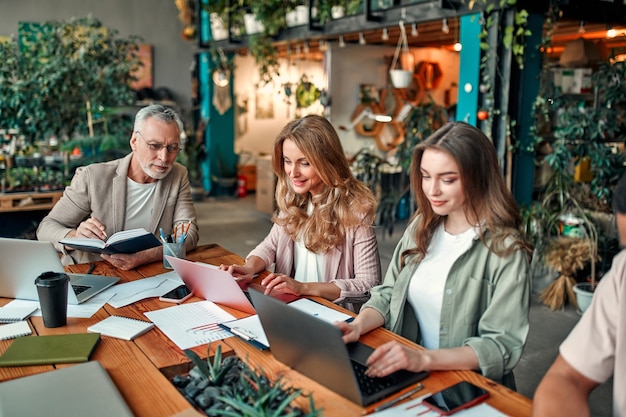 Pessoas criativas multirraciais em um escritório moderno. grupo de jovens empresários e chefe sênior estão trabalhando juntos com laptop, tablet, smartphone, caderno, gráficos. equipe de sucesso em coworking