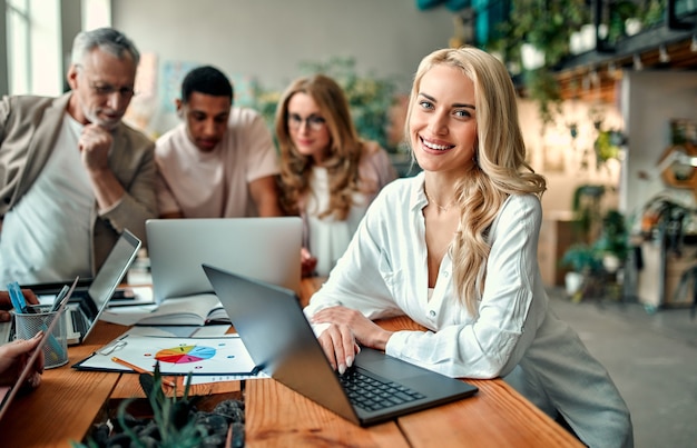 Pessoas criativas multirraciais em um escritório moderno. Grupo de jovens empresários e chefe sênior estão trabalhando juntos com laptop, tablet, smartphone, caderno, gráficos. Equipe de sucesso em coworking