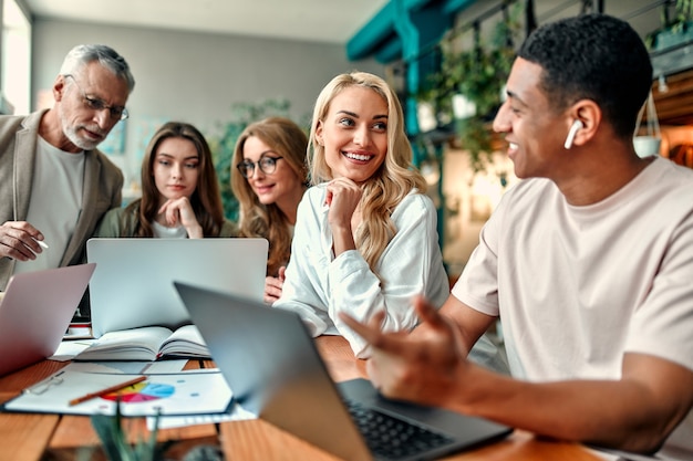 Pessoas criativas multirraciais em um escritório moderno. grupo de jovens empresários e chefe sênior estão trabalhando juntos com laptop, tablet, smartphone, caderno, gráficos. equipe de sucesso em coworking