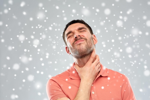 Pessoas, cuidados de saúde, inverno, natal e conceito de problema - homem infeliz tocando seu pescoço e sofrendo de dor de garganta sobre neve em fundo cinza